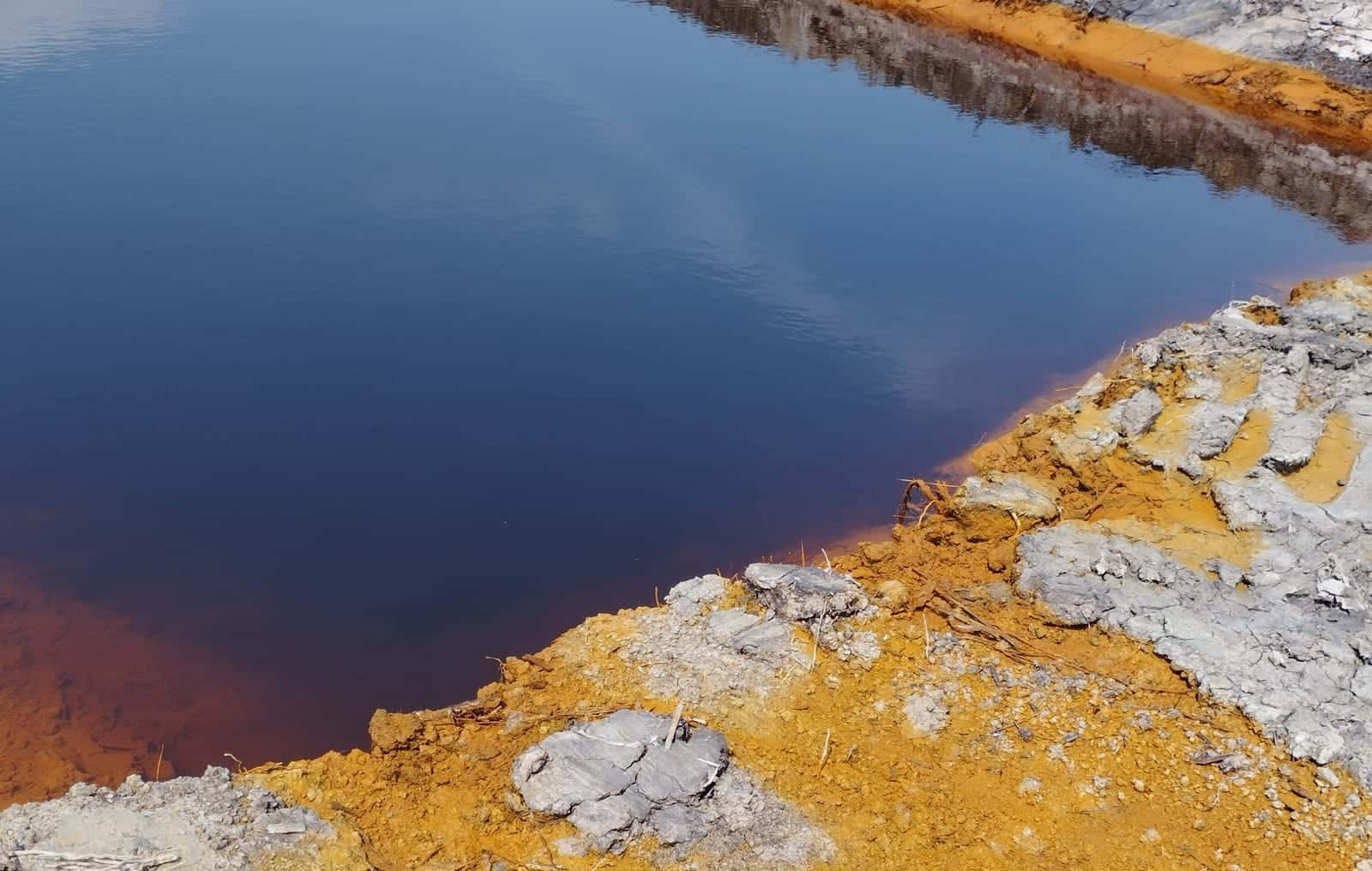 Ditch water and soil stained rust-orange, the signature of active acid sulfate soil